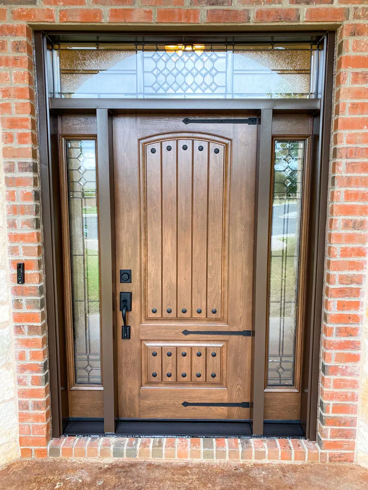 New wood-look entry door with glass sidelights in a brick wall