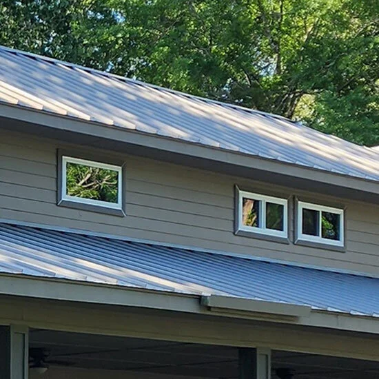 Small windows set high in a gray-sided wall under a metal roof