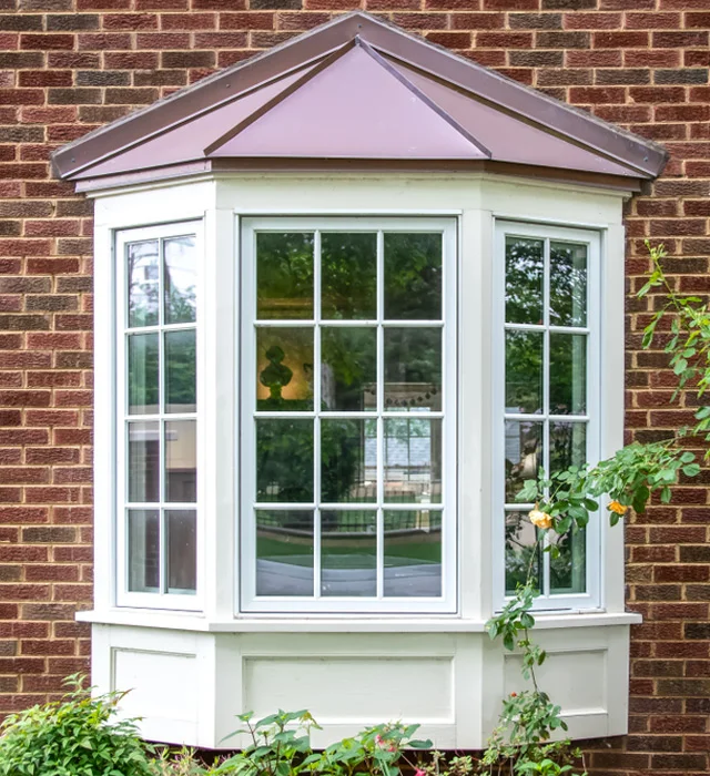 Bay window with white grids and a copper roof on a brick house