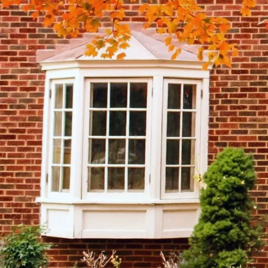 Bay window with white grids on a red brick house under fall leaves