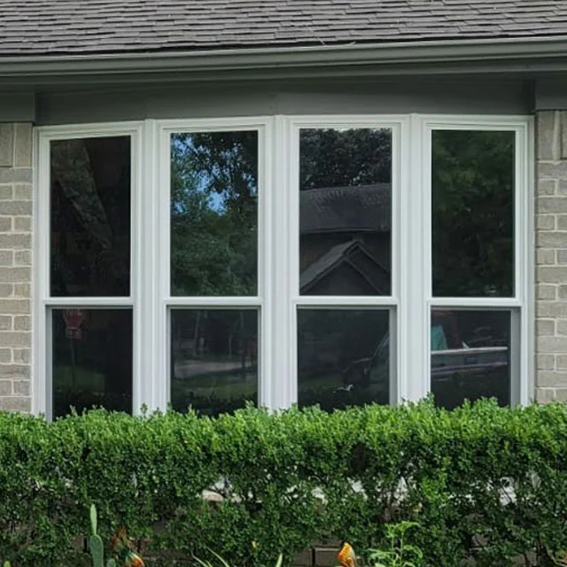 Four-pane bow window with white frames above a trimmed hedge