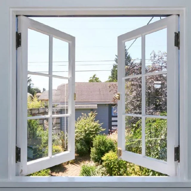 Pair of white casement windows swung open onto a backyard garden