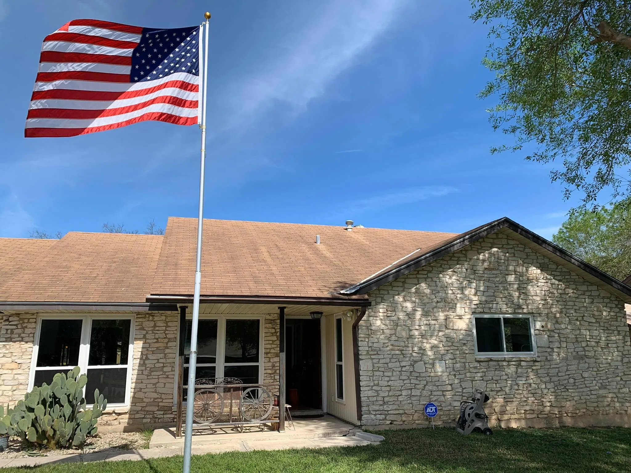Stone ranch home with new windows and a flagpole in the yard