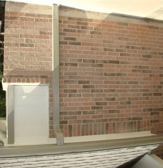 Downspout running down a brick wall beside a small white wall section