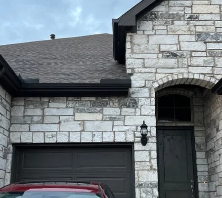 Stone home with black gutters and downspouts above the garage and front door