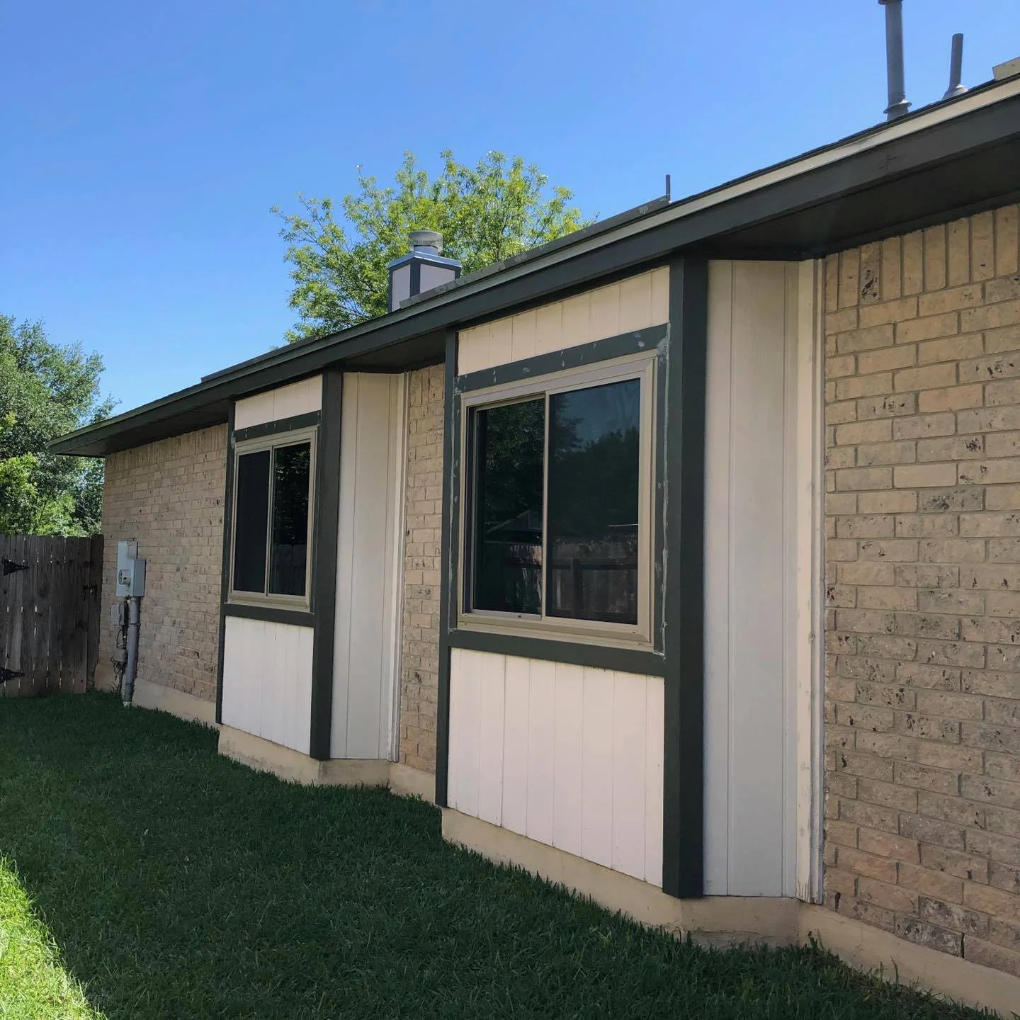 Side of a one-story brick house with two sliding windows set in painted panel bays