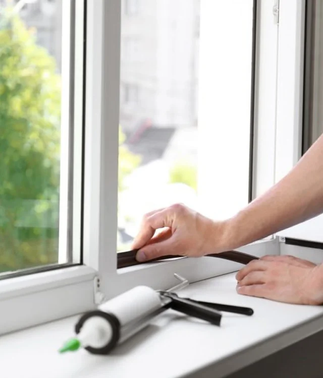 Hands sealing the frame of a new window with a caulk gun