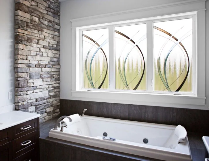Bathroom with a jetted tub under three windows with decorative glass