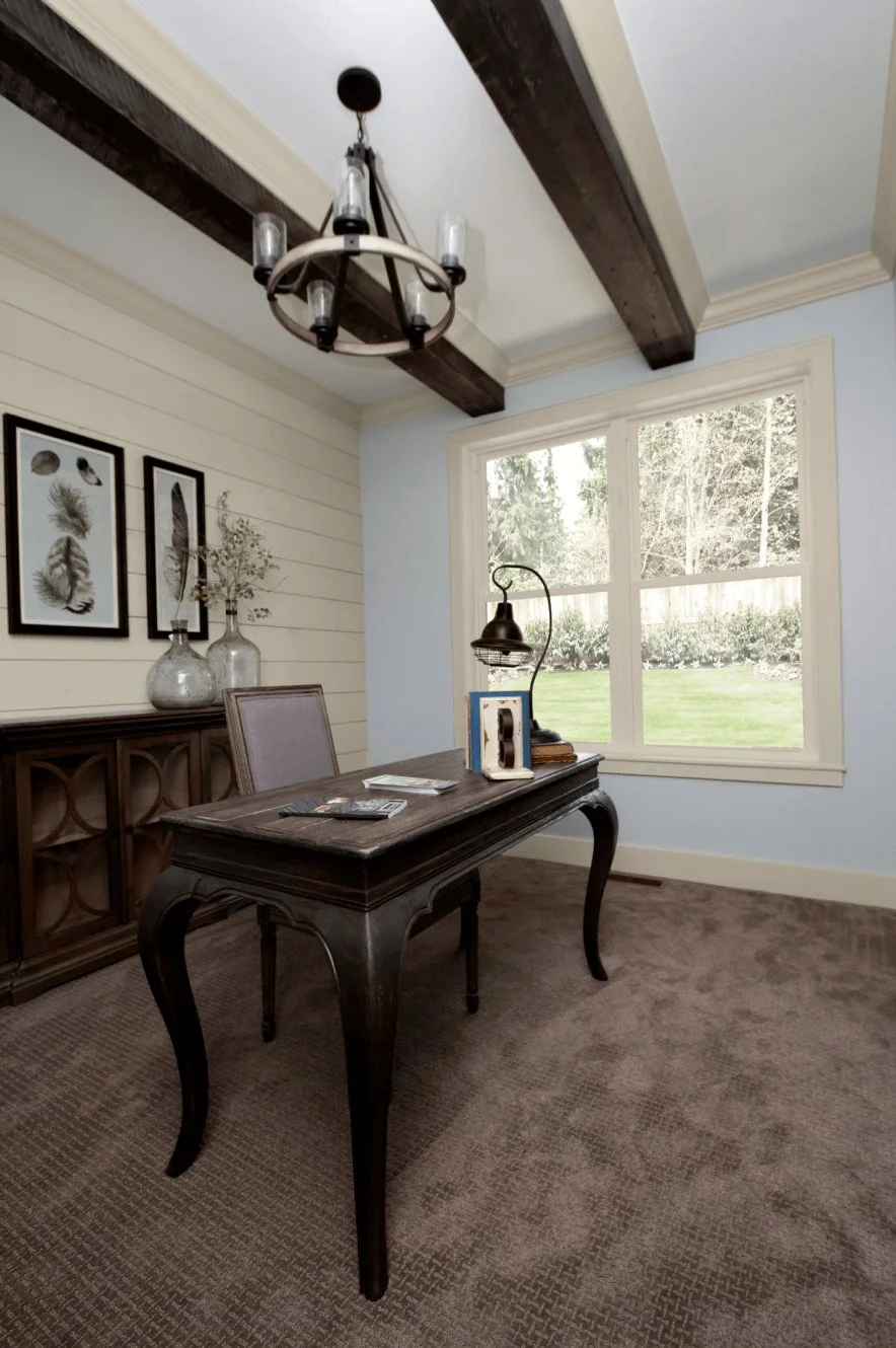 Home office with a wood desk under a beamed ceiling and a window