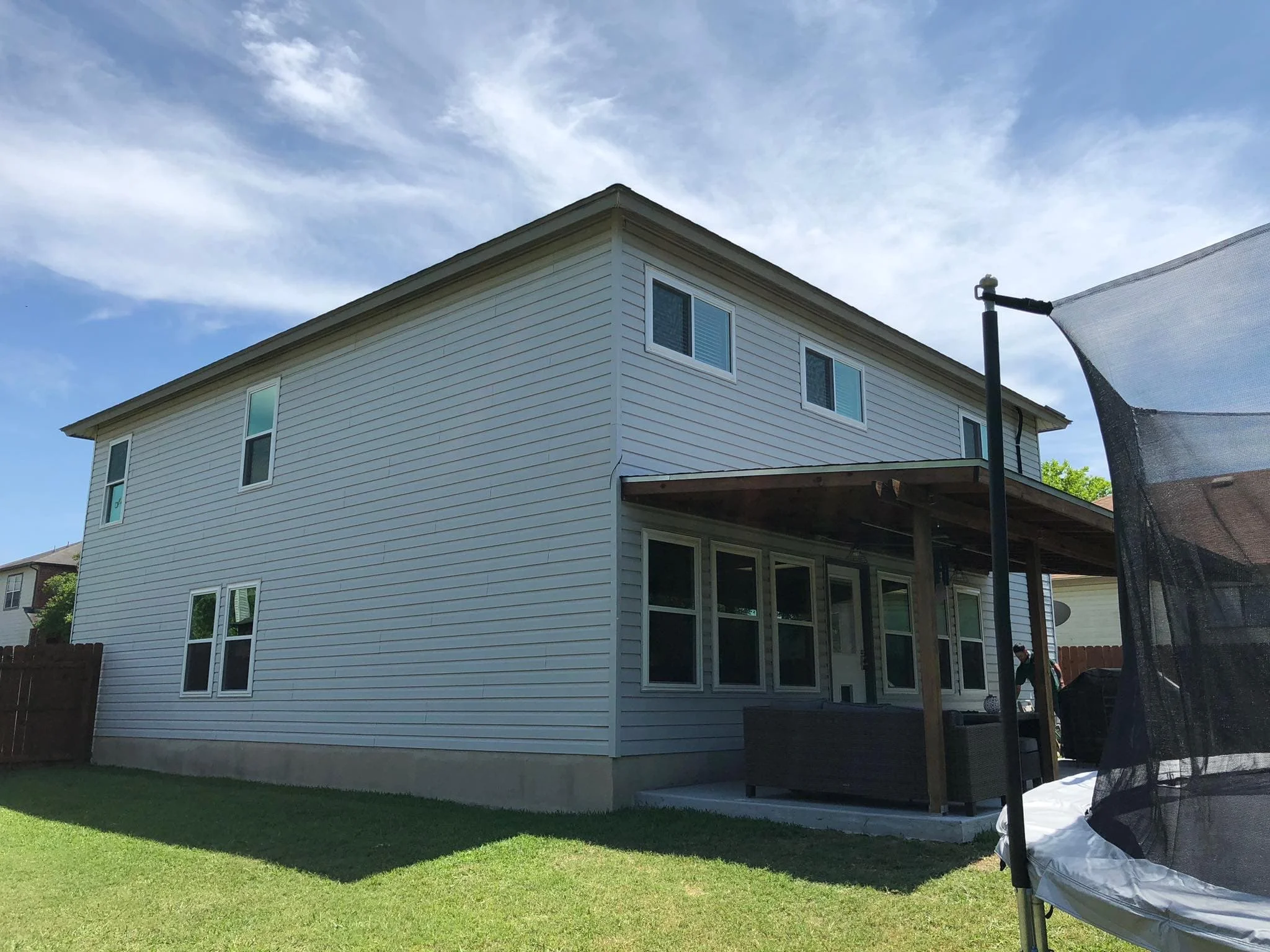 Back of a two-story house with pale blue-gray siding, white-framed windows and a covered patio