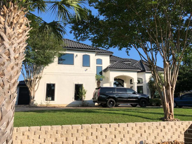 White stucco home with new windows behind palm trees and a stone wall