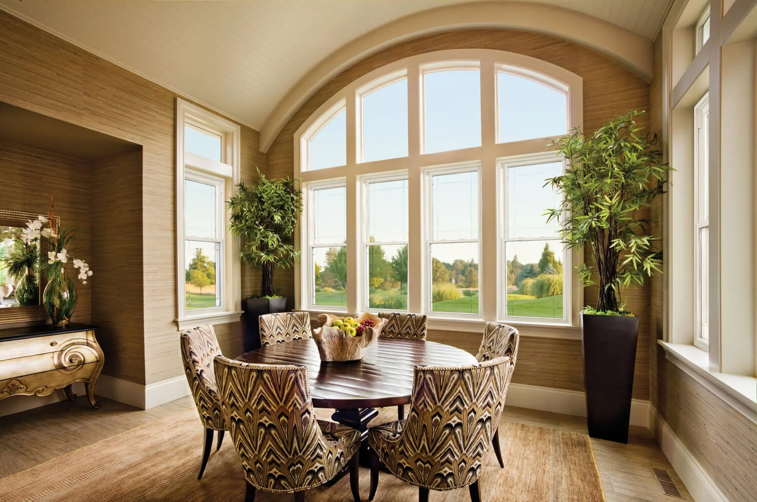 Dining room with a row of white double-hung windows under an arched transom, looking out on a lawn and trees