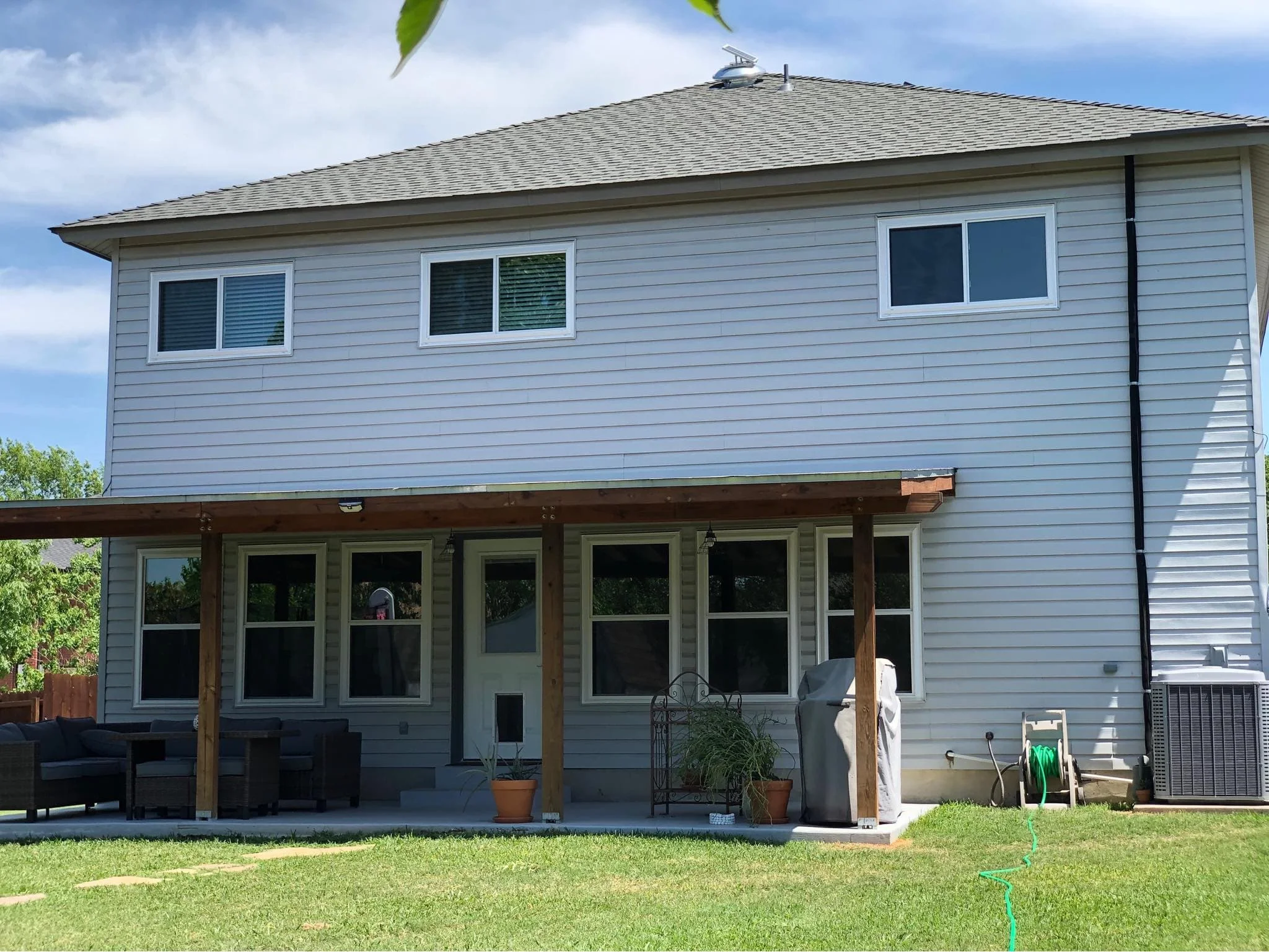 Back of a two-story house with vinyl siding, white-framed windows and a covered patio