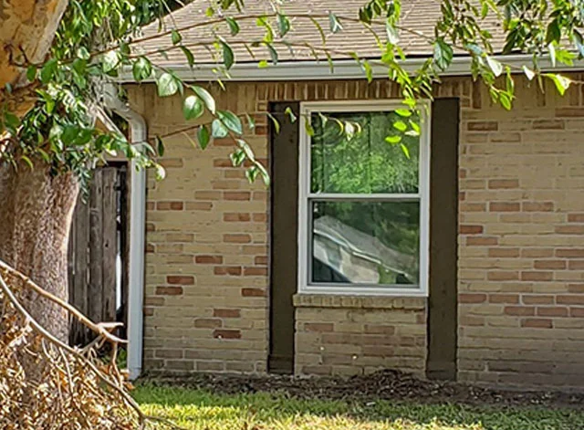 White single-hung window in a tan brick wall between dark trim boards