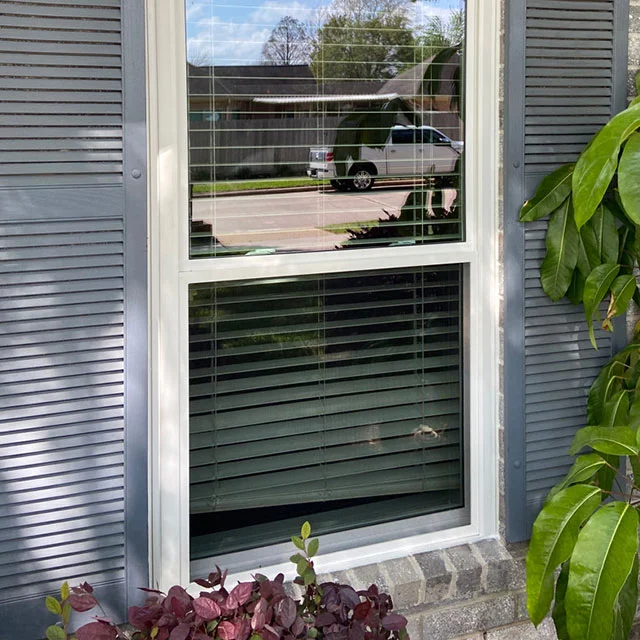 White single-hung window between gray louvered shutters on a gray-sided house