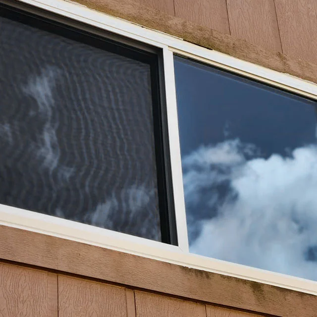 Slider window in wood siding, with clouds reflected in the glass