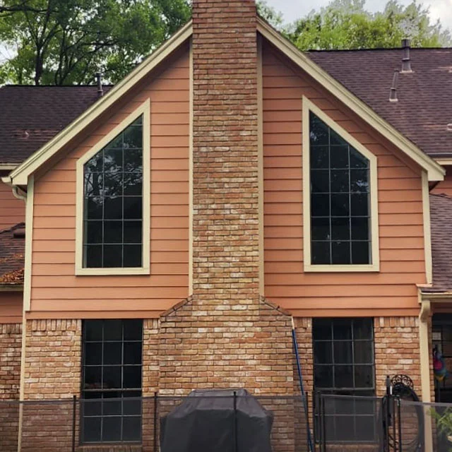 Two angled specialty shaped windows with grids on either side of a brick chimney