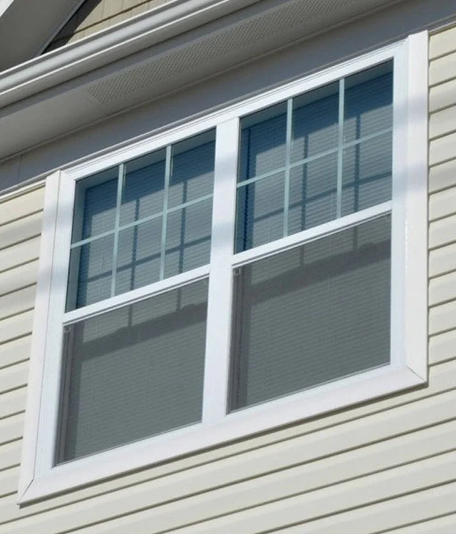 White hung window with grids in the upper sash, set in beige siding