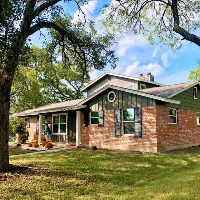 Brick and green siding home with new windows under large oak trees