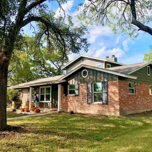 Brick and siding home with new windows, seen through the trees
