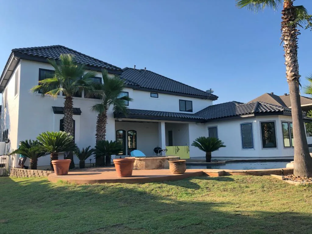 Two-story stucco home with a tile roof and new windows facing a backyard patio