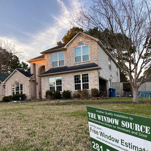Two-story light brick house with white grid windows and a Window Source yard sign on the front lawn