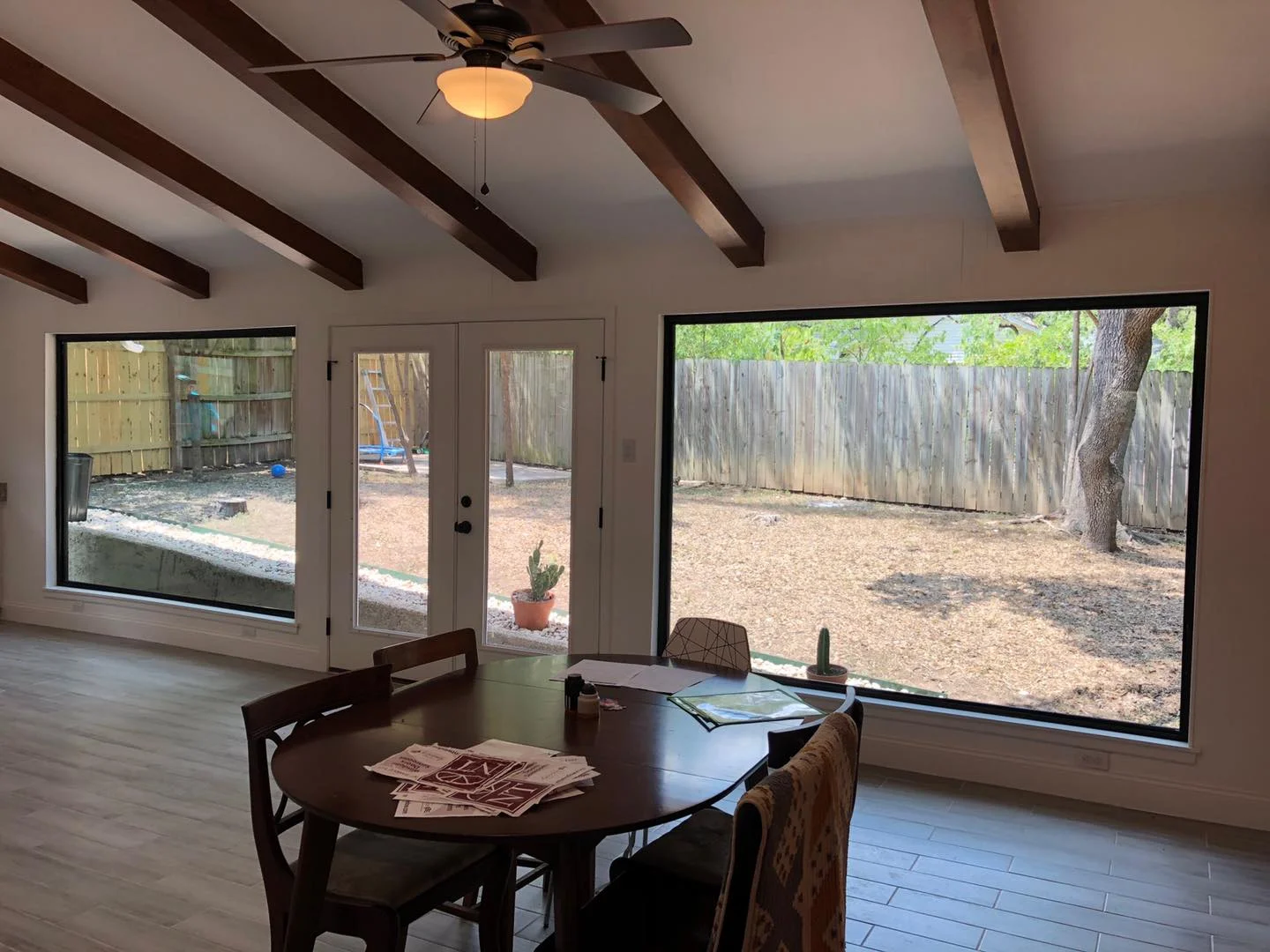 Dining room with wood ceiling beams, two large black-framed picture windows and a pair of French doors to the backyard